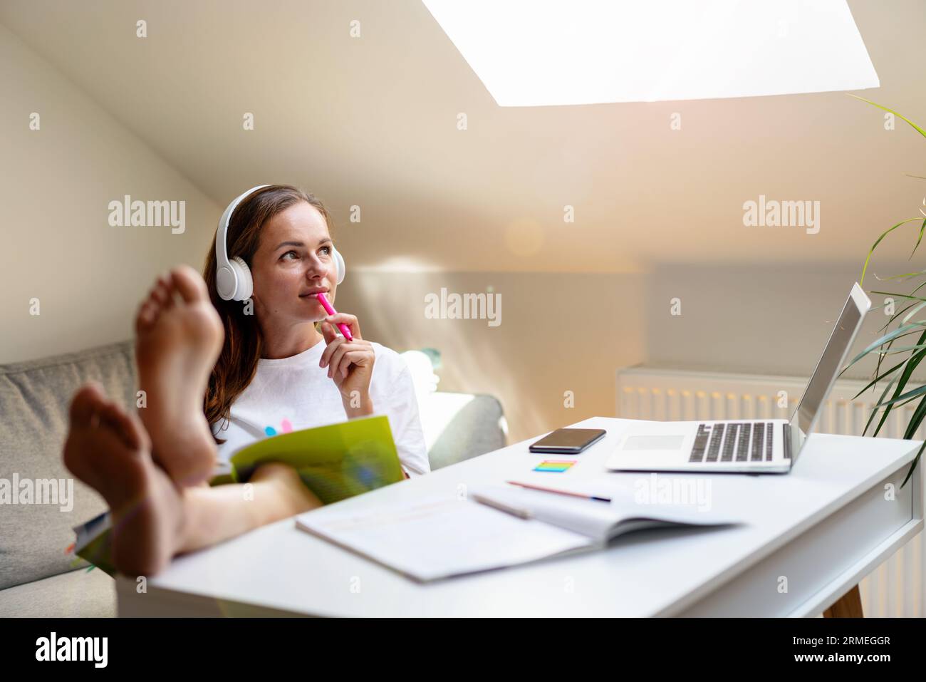 Donna in cuffia seduta al tavolo a casa, che legge un libro di testo universitario e pensa al suo futuro. Foto Stock