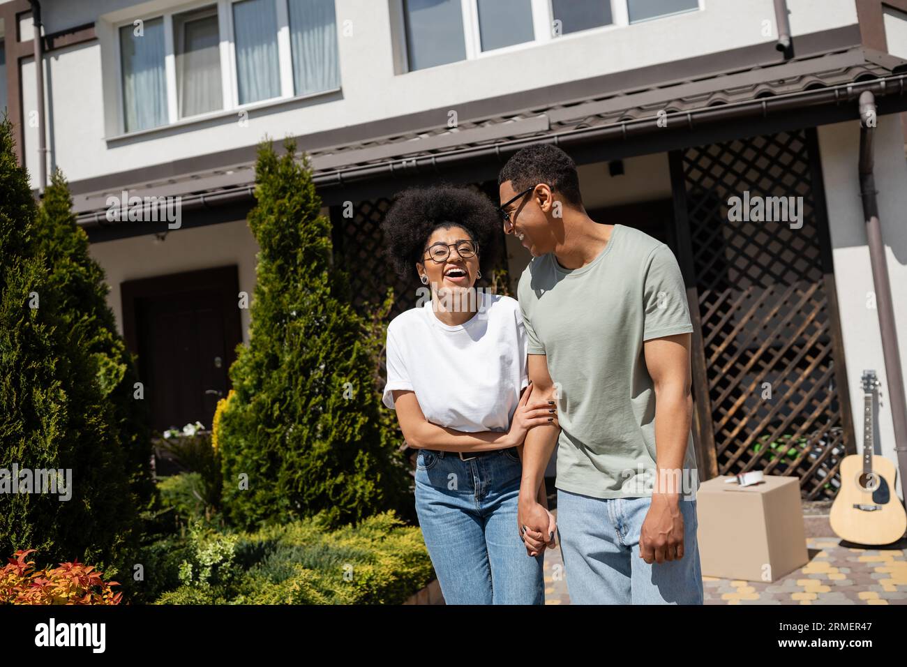 eccitata donna afroamericana in piedi vicino al fidanzato e nuova casa sullo sfondo all'aperto Foto Stock