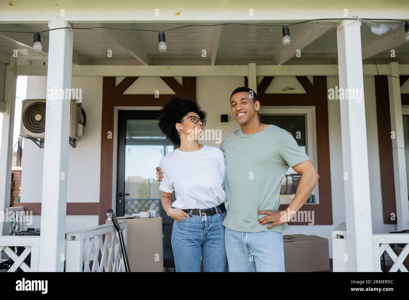 sorridente coppia afroamericana che si abbraccia mentre si trova sul portico di una nuova casa Foto Stock