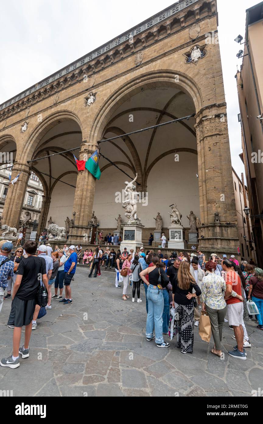 I turisti si riuniscono in Piazza della Signoria di fronte agli ampi archi della Loggia del Lani, un museo di scultura all'aperto accanto agli Uffizi gal Foto Stock