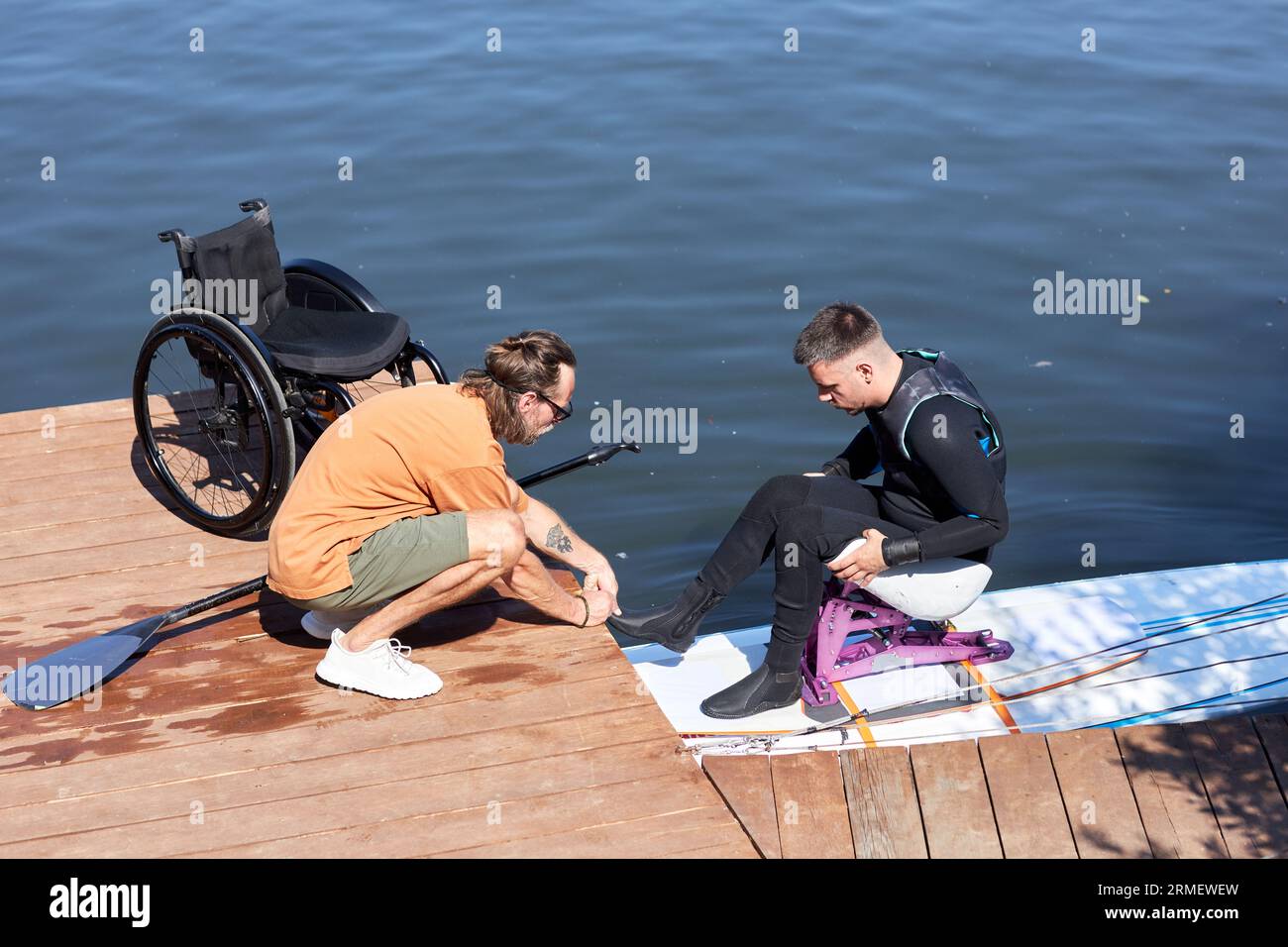 Ritratto laterale dell'istruttore che assiste l'uomo con disabilità, wakeboard con attrezzature adattive Foto Stock