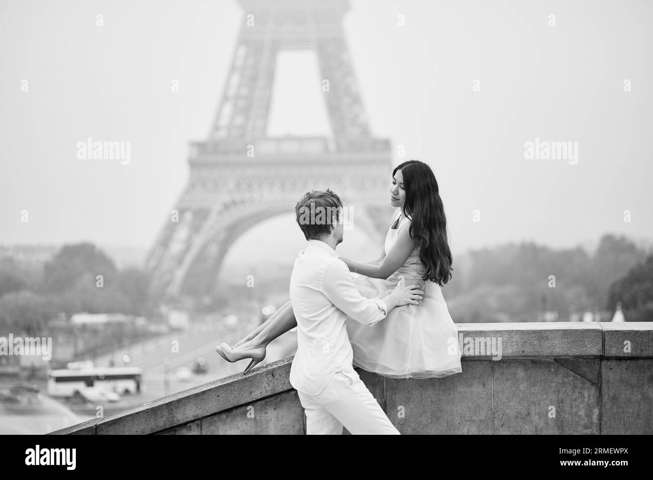 Bellissima coppia romantica innamorata vicino alla Torre Eiffel a Parigi in una giornata piovosa e nebbiosa, immagine in bianco e nero Foto Stock