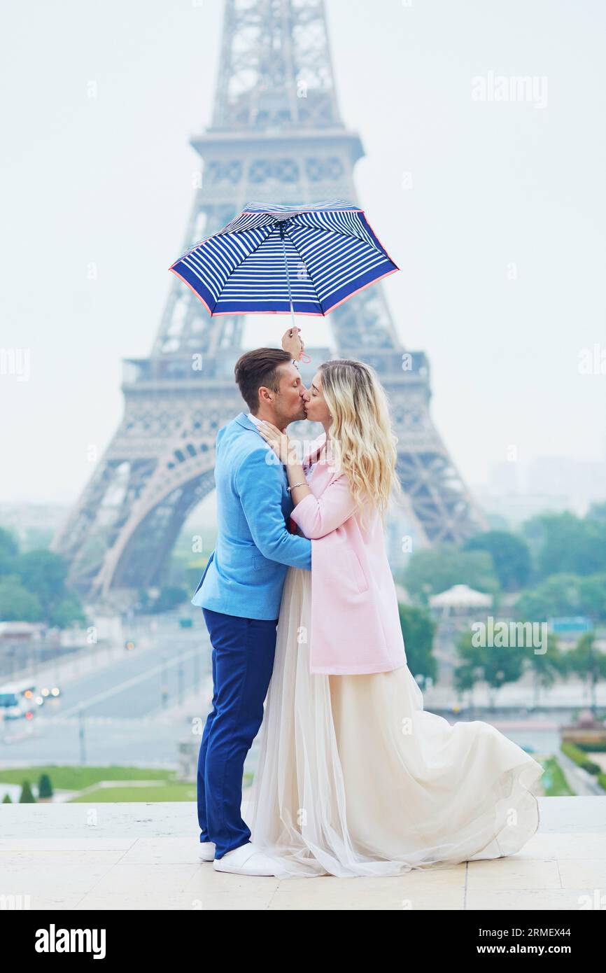 Appena sposata sotto ombrello in caso di pioggia vicino alla Torre Eiffel il giorno del loro matrimonio. Sposo e sposo a Parigi, in Francia Foto Stock