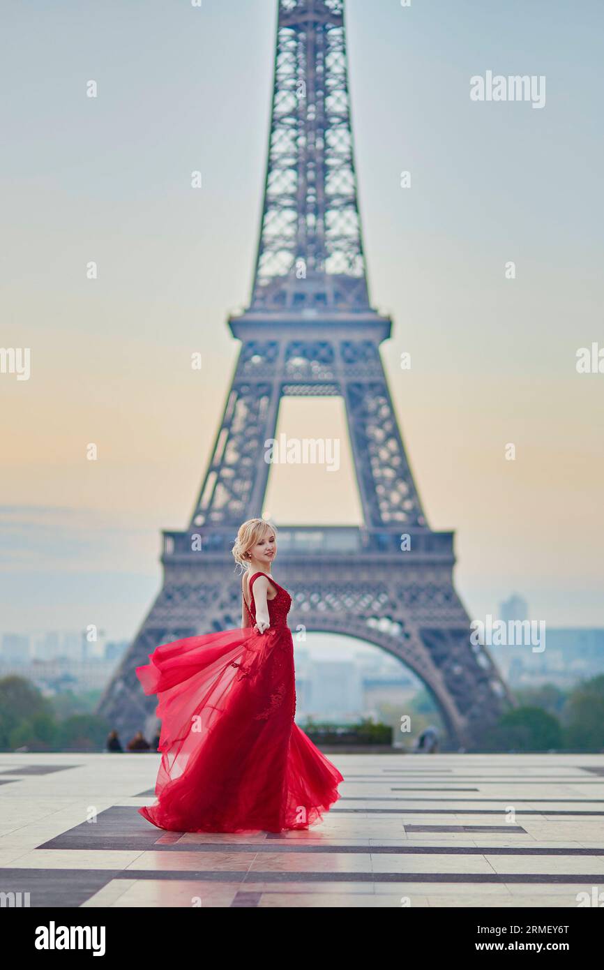 Bella giovane donna in lungo vestito rosso che balla vicino alla Torre Eiffel a Parigi, in Francia Foto Stock