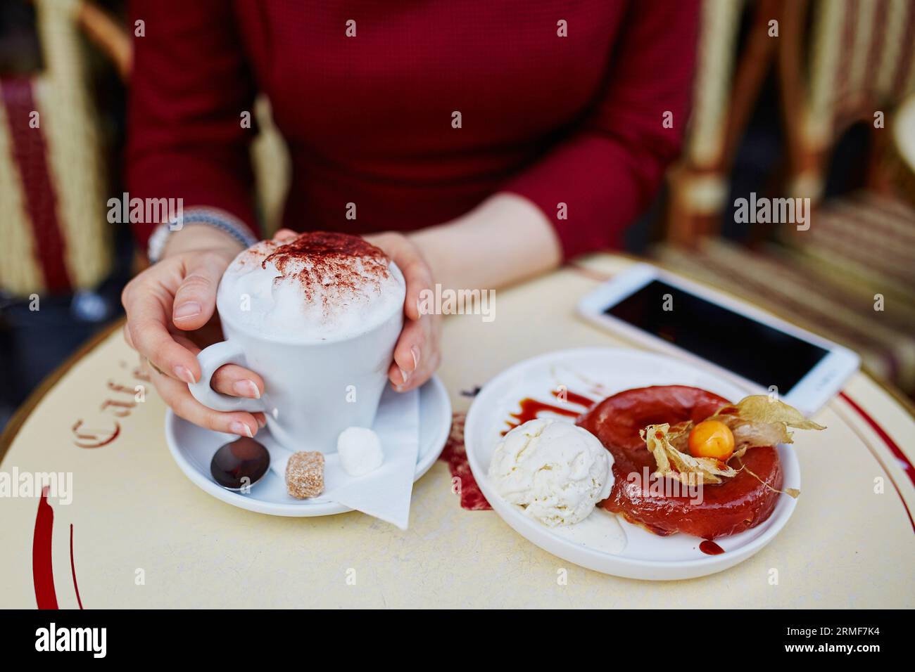 Primo piano delle mani di una donna con il telefono cellulare, una tazza di caffè e una torta nella caffetteria all'aperto parigina Foto Stock
