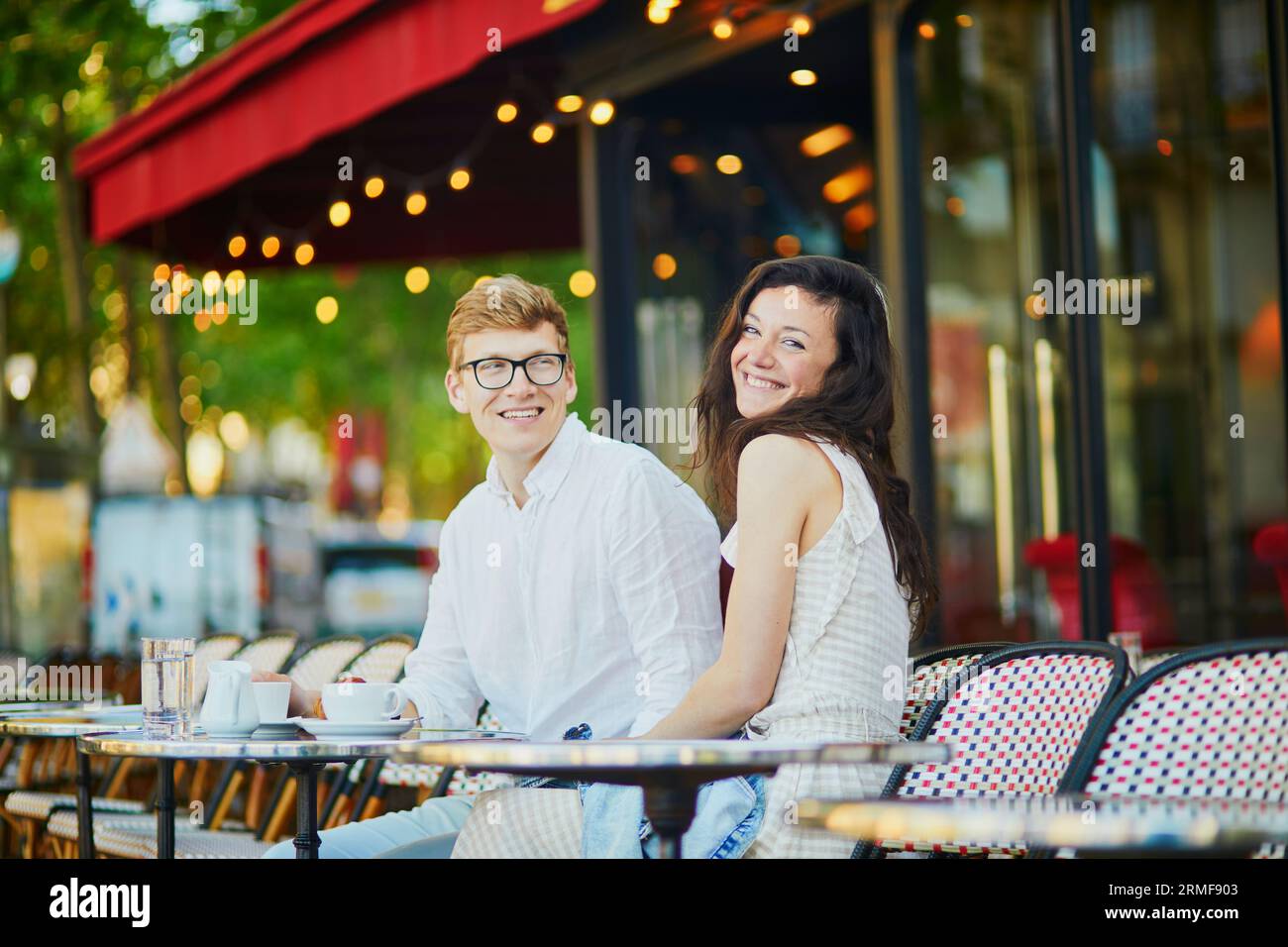 Felice coppia romantica a Parigi, sorseggiando un caffè nel tradizionale caffè all'aperto parigino. Turisti che trascorrono le loro vacanze in Francia Foto Stock