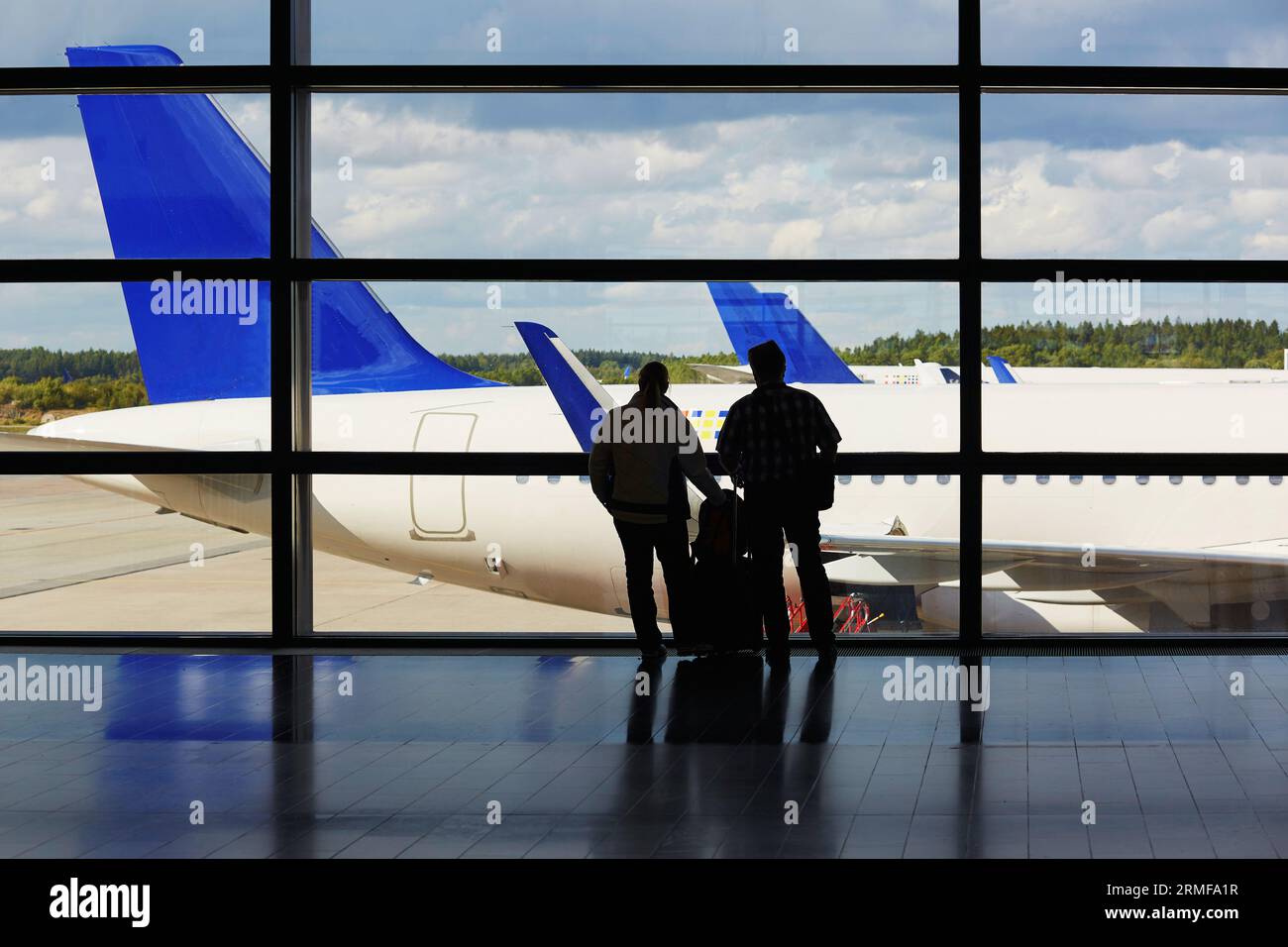Sagome di una coppia con bagaglio a mano in aeroporto, guardando l'aereo dalla finestra Foto Stock