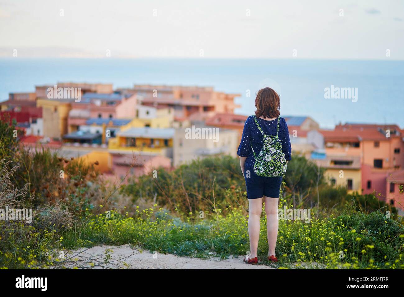 Ragazza turistica con zaino che gode di una splendida vista sul villaggio di Castelsardo in Sardegna Foto Stock