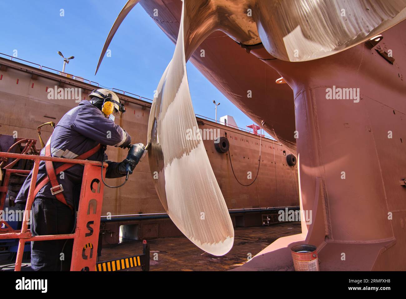 uomo che ripara un'elica di una nave utilizzando una sega manuale .propeller manutenzione della nave. bacino di carenaggio. Foto Stock