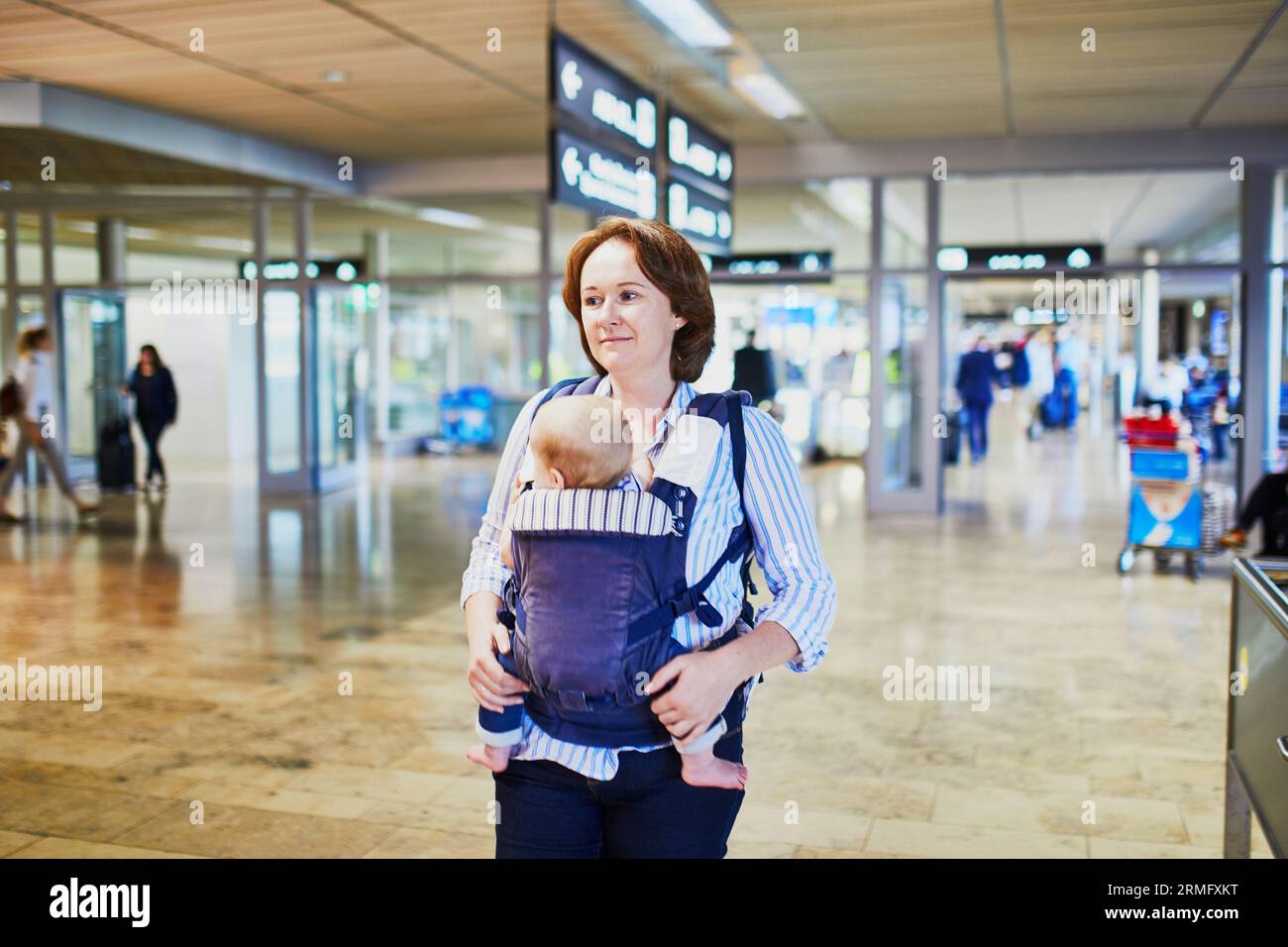 Donna con bambina nel portabandiera all'aeroporto internazionale. Madre con bambino che cammina fino al cancello. Viaggiare con i bambini Foto Stock
