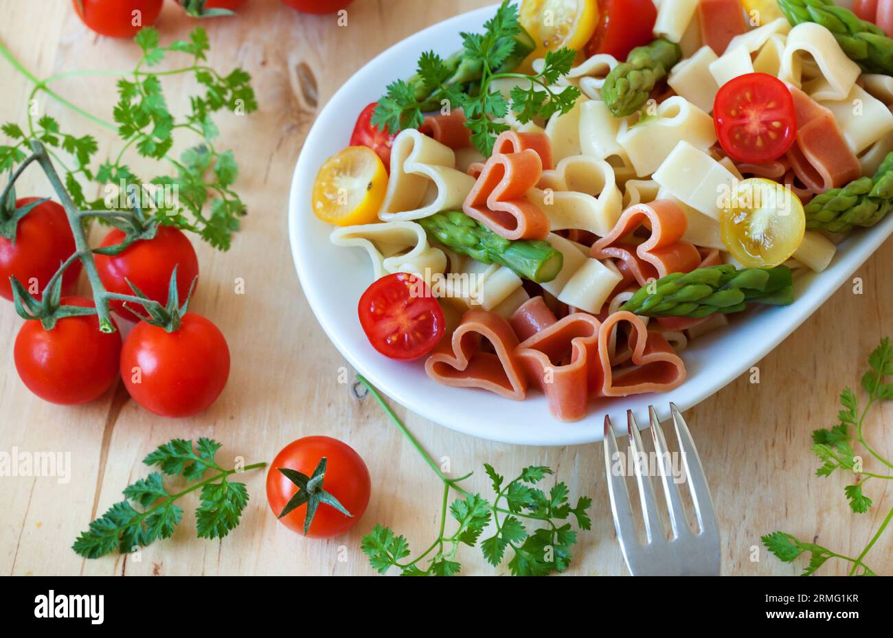 Cena romantica. Deliziosa pasta a forma di cuore con pomodori, asparagi ed erbe fresche Foto Stock