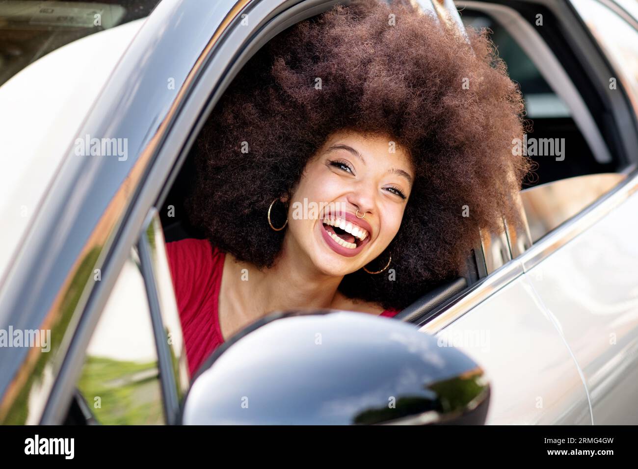 Ritratto di una giovane donna afroamericana in un panno casual con capelli afro sorridenti e guardando la fotocamera mentre si guida una nuova auto Foto Stock