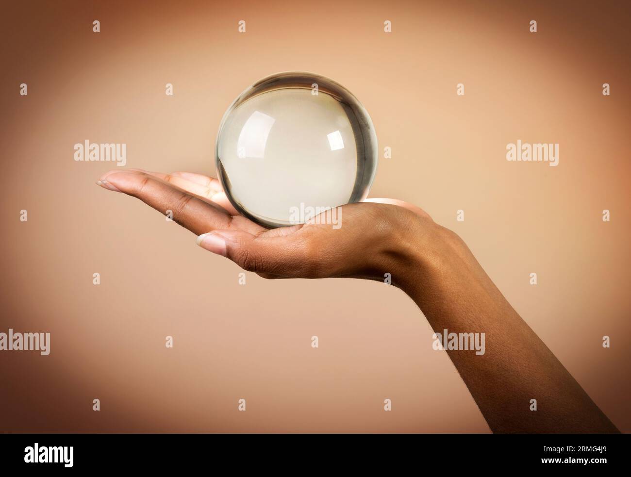 Coltiva la mano non riconoscibile di una donna afroamericana che tiene la sfera di cristallo su sfondo beige Foto Stock