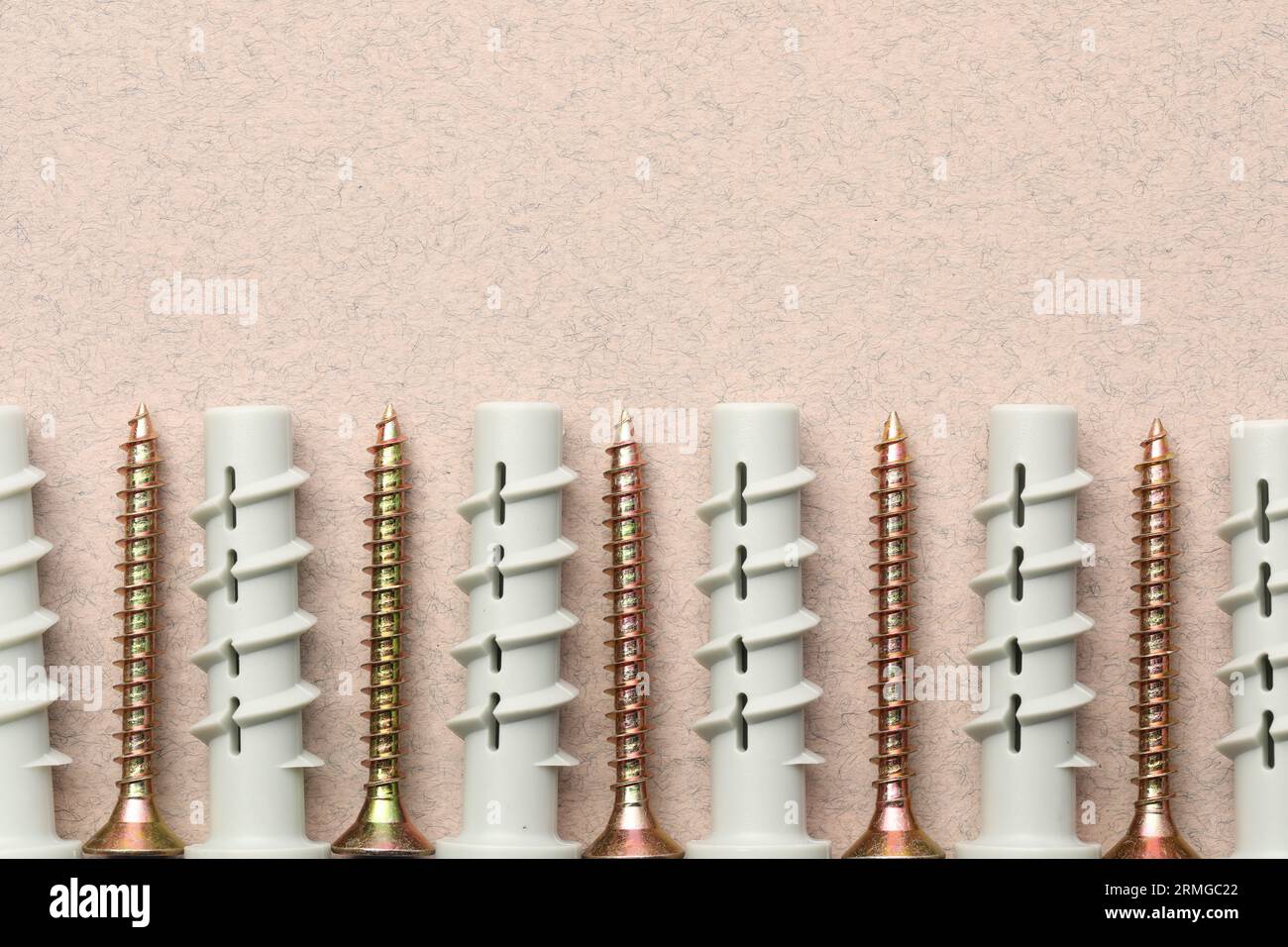 Molte viti e tasselli in metallo su un tavolo ruvido beige, posizionamento piatto. Spazio per il testo Foto Stock