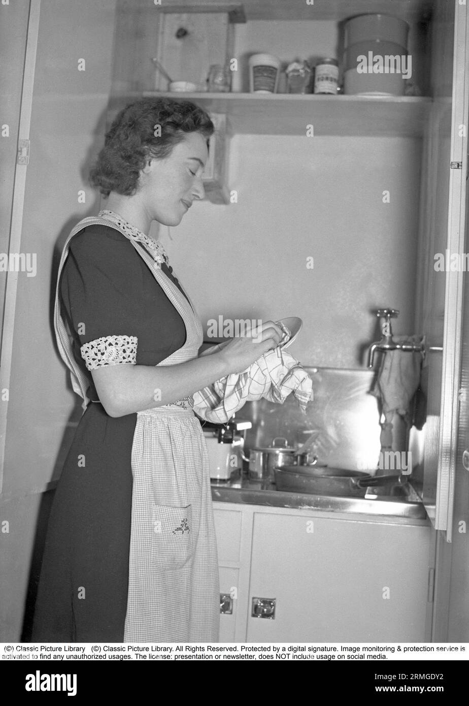 Cucina negli anni '1940 Una donna si vede in cucina asciugare un piatto di porcellana che ha pulito. Svezia 1940. Kristoffersson rif. 54-5 Foto Stock