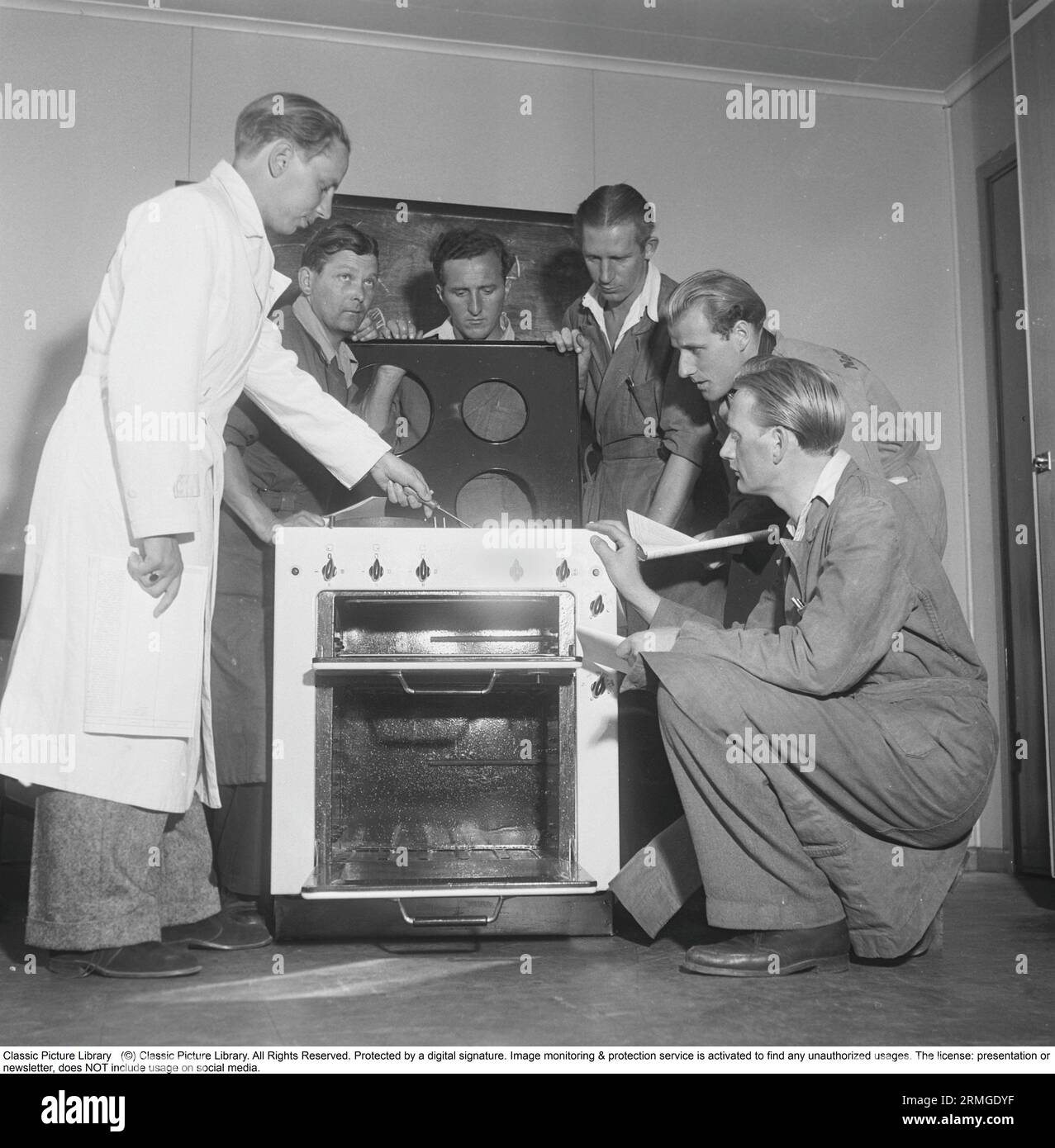 Negli anni '1950 Un uomo in una cucina elettrica del produttore svedese Husqvarna, con un cappotto bianco per tecnici, istruisce un gruppo di militari sui dettagli e le caratteristiche della nuova stufa. Svezia 1950. Kristoffersson rif. AZ69-10 Foto Stock