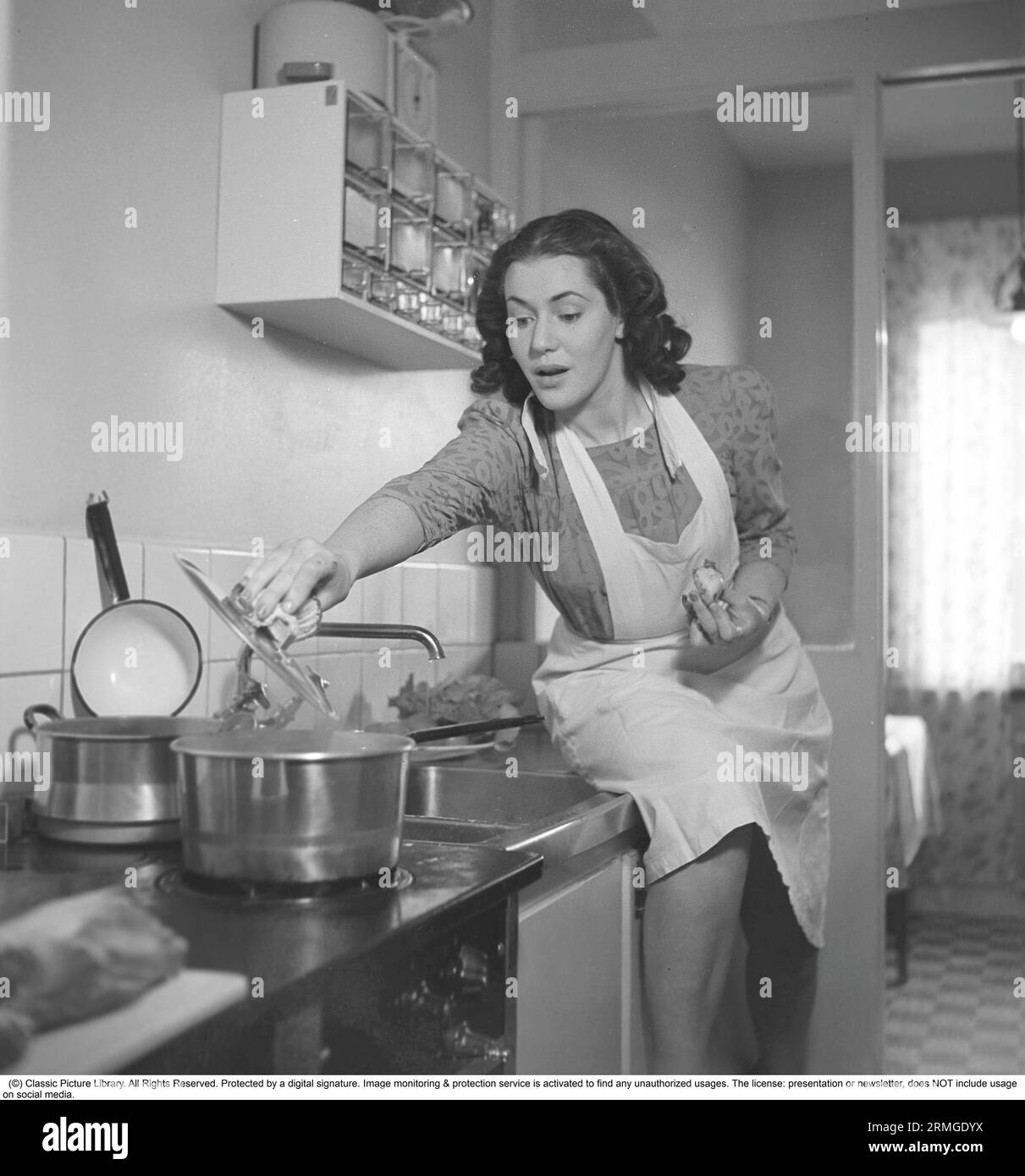 In cucina anni '1940 Interno di una cucina e una giovane donna che solleva il coperchio di una pentola sul fornello, bollendo al vapore. È l'attrice Eivor Landström, 1919-2004. Svezia 1940 Kristoffersson rif 158-34 Foto Stock