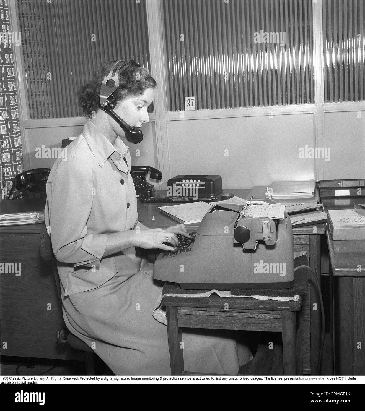 Una ragazza d'ufficio negli anni '1940 Una giovane donna siede alla macchina da scrivere e scrive. Ha le cuffie e un microfono. Forse gestisce anche il centralino dell'azienda o può anche ascoltare una registrazione del messaggio di qualcuno e annotarlo. La macchina da scrivere è elettrica. Svezia 1946. Kristoffersson BM72-1 Foto Stock