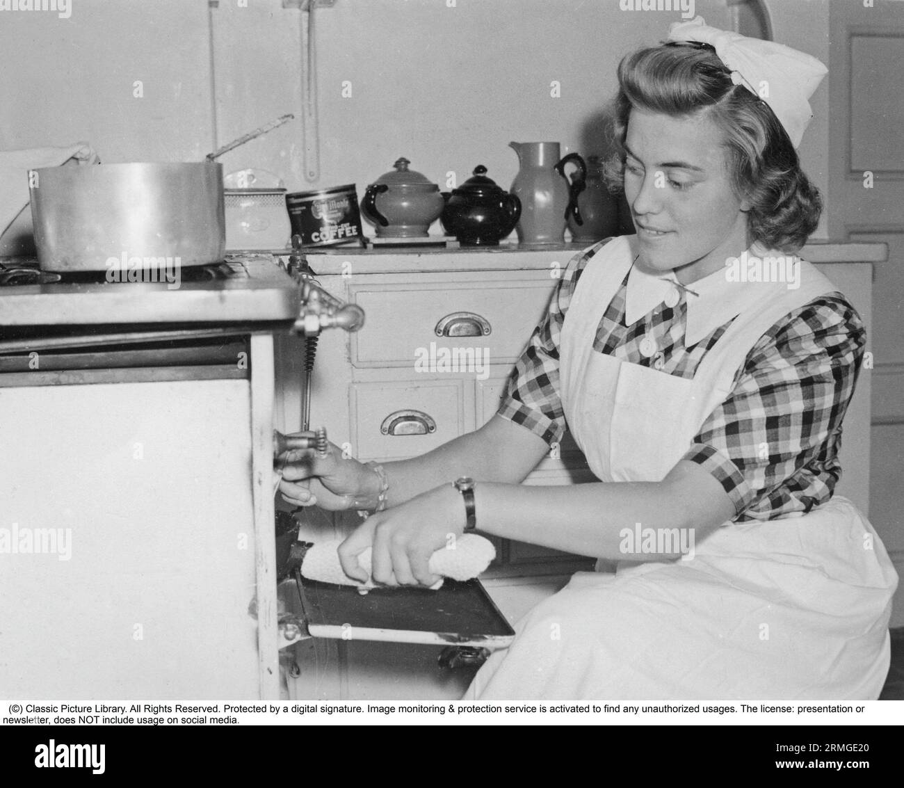 Cucinare negli anni '1940 Una giovane donna impiegata come cameriera di casa sta cucinando un pasto sul fornello della cucina e ha qualcosa nel forno. Svezia 1940. Foto Stock