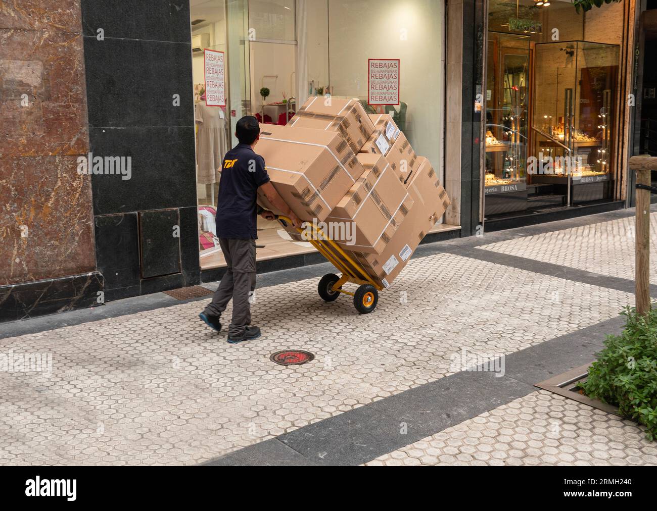 Addetto alle consegne in strada con un sacco di scatole su un carrello a mano. Non riesce a vedere avanti per i pacchi.. San Sebastian, Spagna - 11 luglio 2023. Foto Stock
