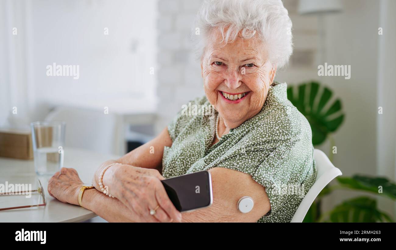 Paziente anziano diabetico che controlla il livello di glucosio nel sangue a domicilio utilizzando un monitor continuo per la glicemia. Foto Stock