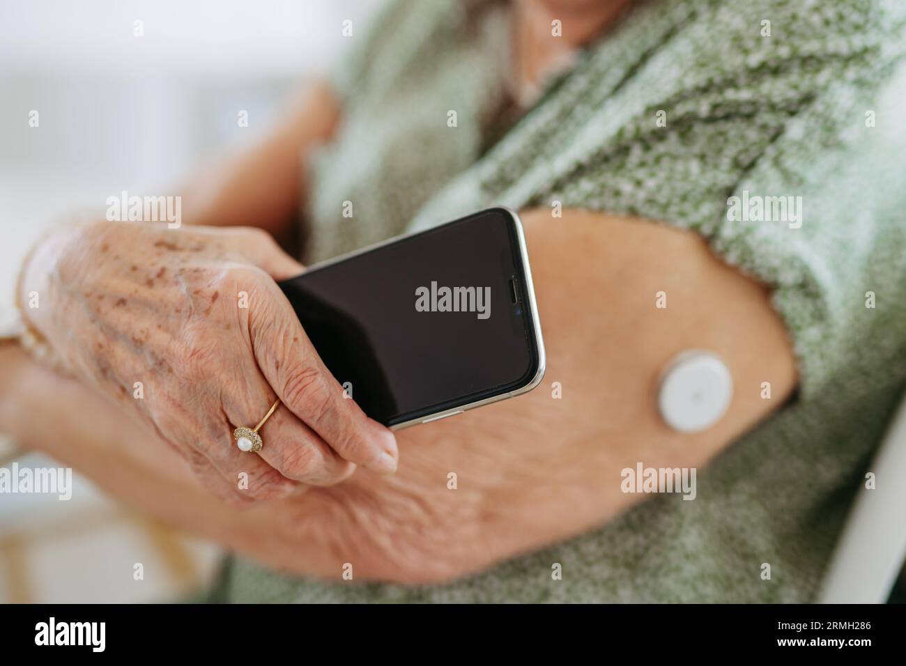 Primo piano del paziente diabetico anziano che controlla il livello di glucosio nel sangue a casa utilizzando il monitor continuo della glicemia. Foto Stock
