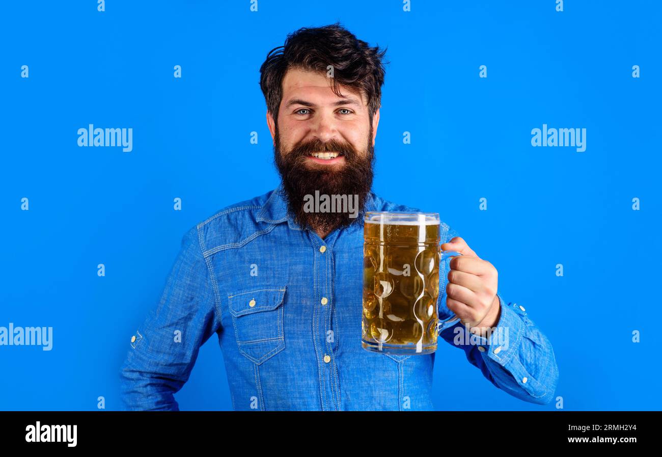 Ora della birra. Uomo barbato sorridente con birra artigianale in tazza al bar o al pub. Tradizione tedesca. Festa dell'Oktoberfest. Uomo elegante in camicia denim che beve Foto Stock