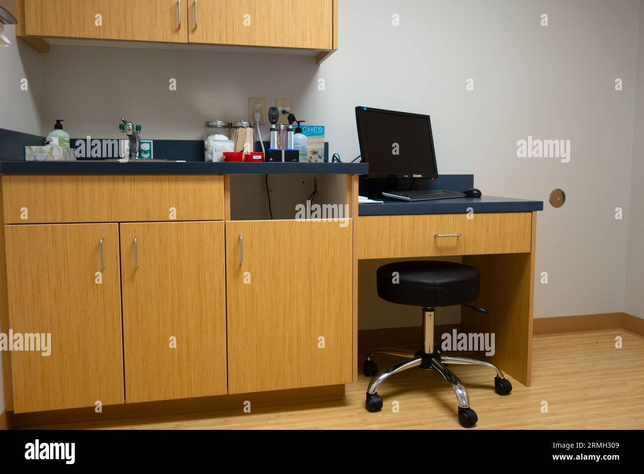 Un computer portatile, sgabello, forniture mediche e armadi, in una sala d'esame di uno studio medico. Foto Stock