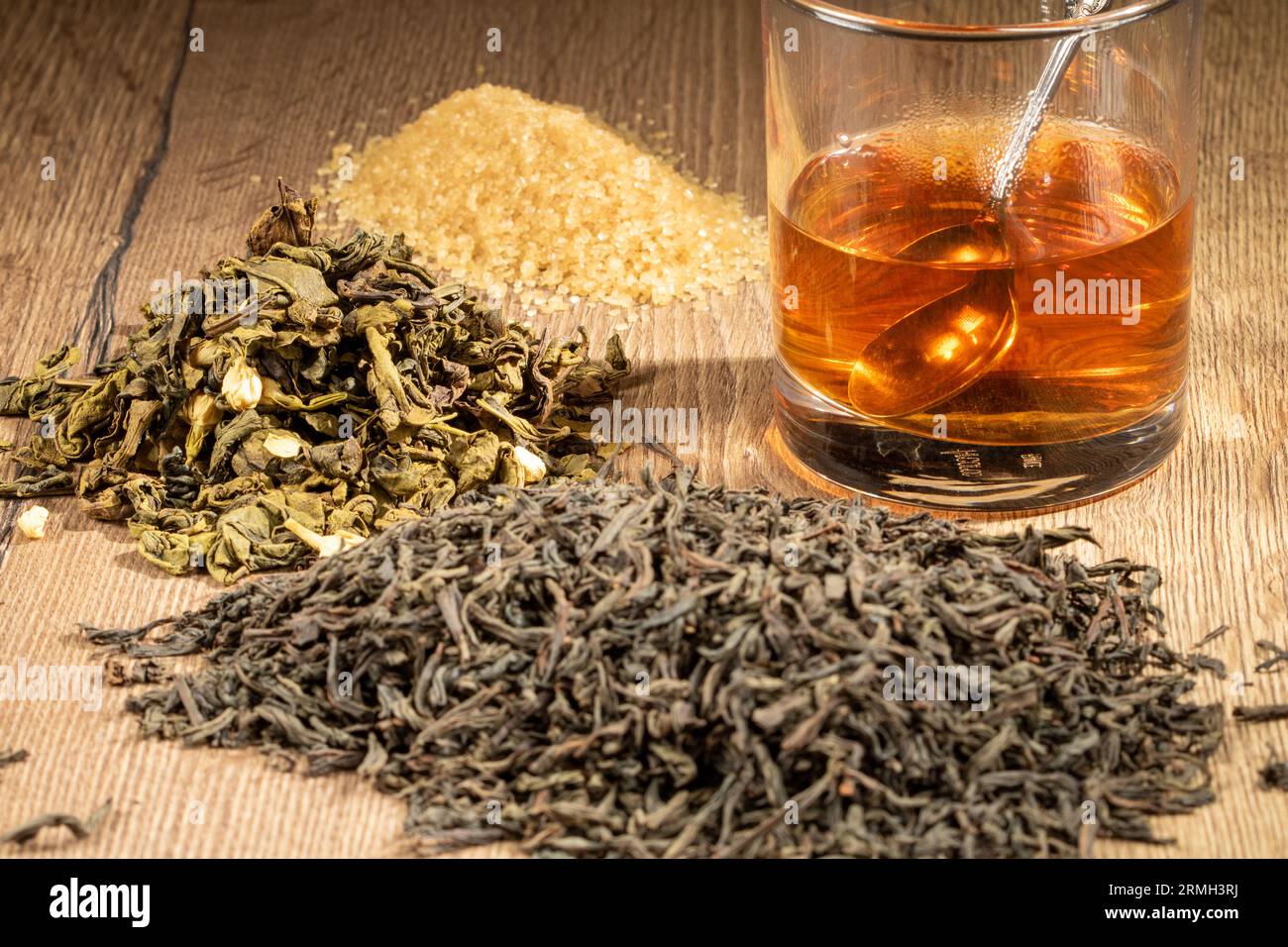 Un mucchio di tè nero e verde secco, un mucchio di zucchero e un bicchiere di tè fresco da vicino. Foto Stock