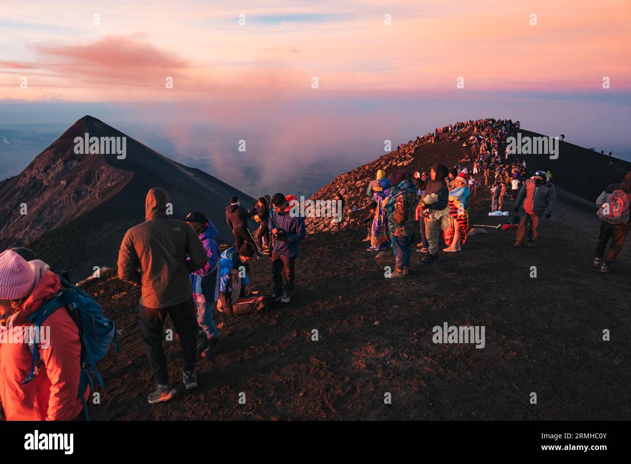 Dozzine di turisti affollano la cima del vulcano Acatenango dormiente in Guatemala per osservare l'adiacente e attivo vulcano Fuego eruttare, all'alba Foto Stock