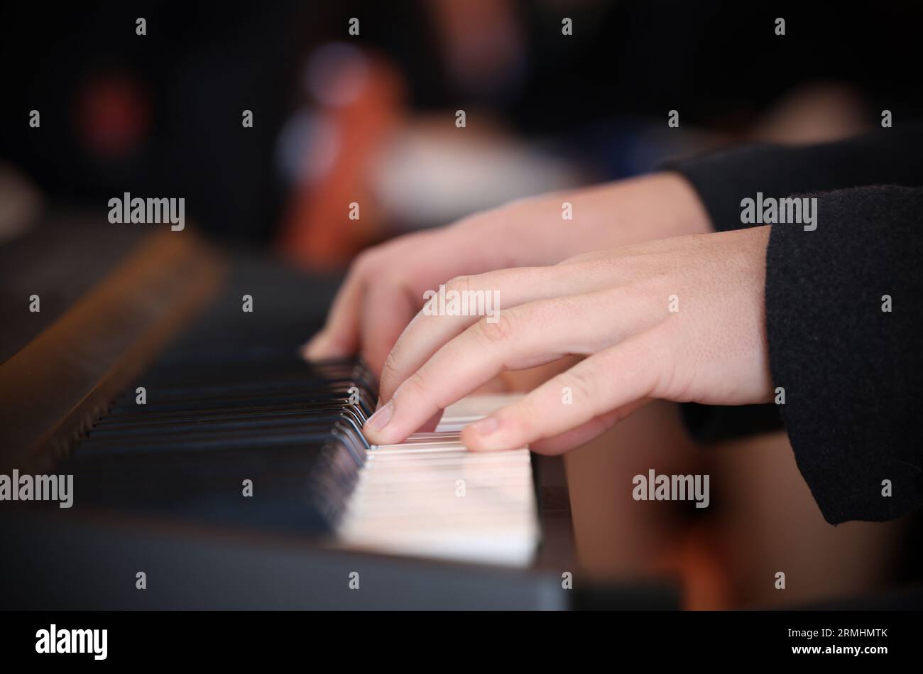 Primo piano di mani e dita che suonano una tastiera o tasti bianchi. Pubblico sfocato sullo sfondo. Mano sinistra a fuoco Foto Stock