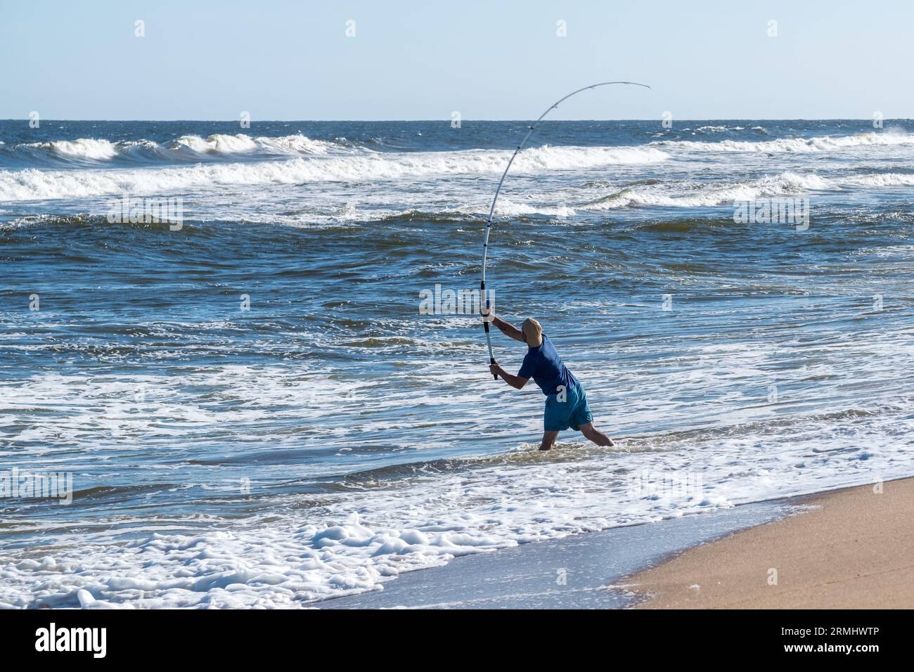 Un giovane pescatore che getta la sua canna da pesca in un oceano impetuoso con forti gonfiori in una soleggiata giornata estiva Foto Stock