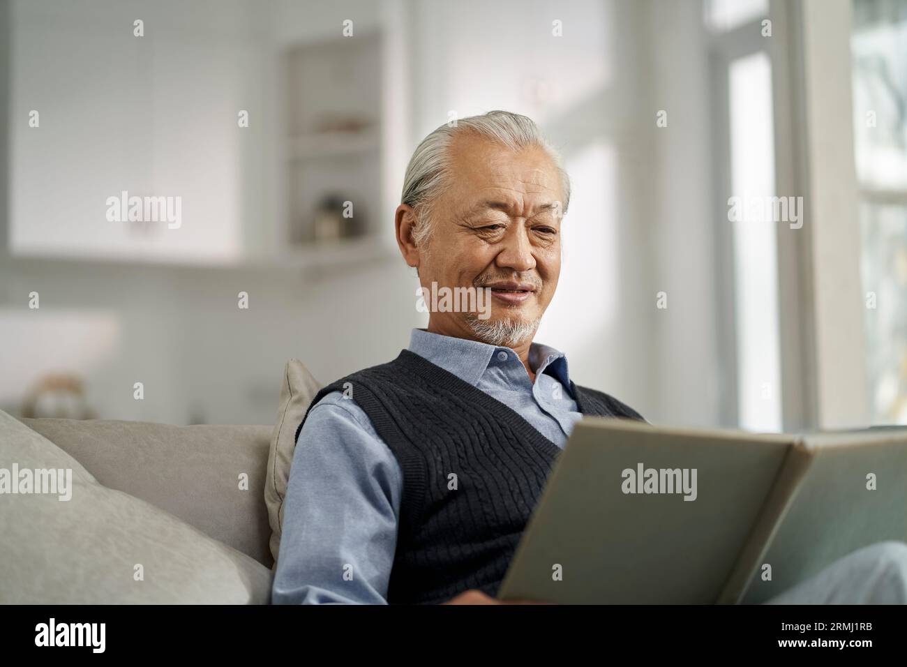 anziano asiatico seduto sul divano in salotto a casa a leggere un libro Foto Stock