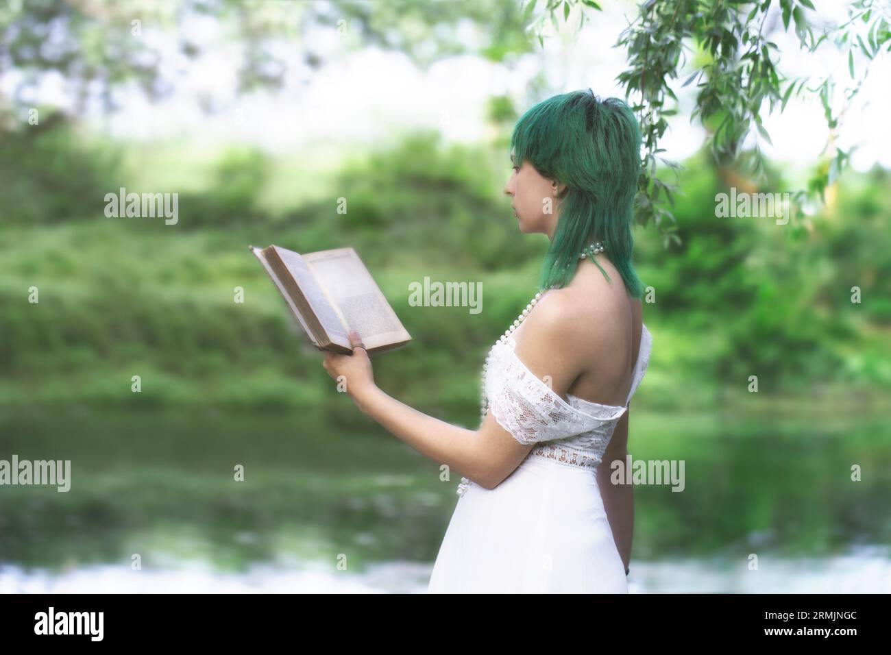 romantica ragazza dai capelli verdi legge un libro in mezzo a un paesaggio verde surreale Foto Stock