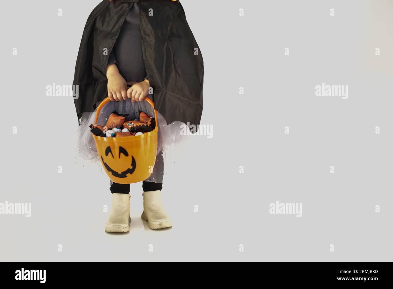 Bambina vestita da strega che tiene il cesto di Halloween pieno di dolci, sfondo bianco. Foto Stock