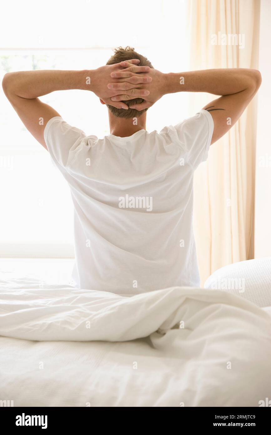 Giovane uomo seduto nel letto stretching Foto Stock