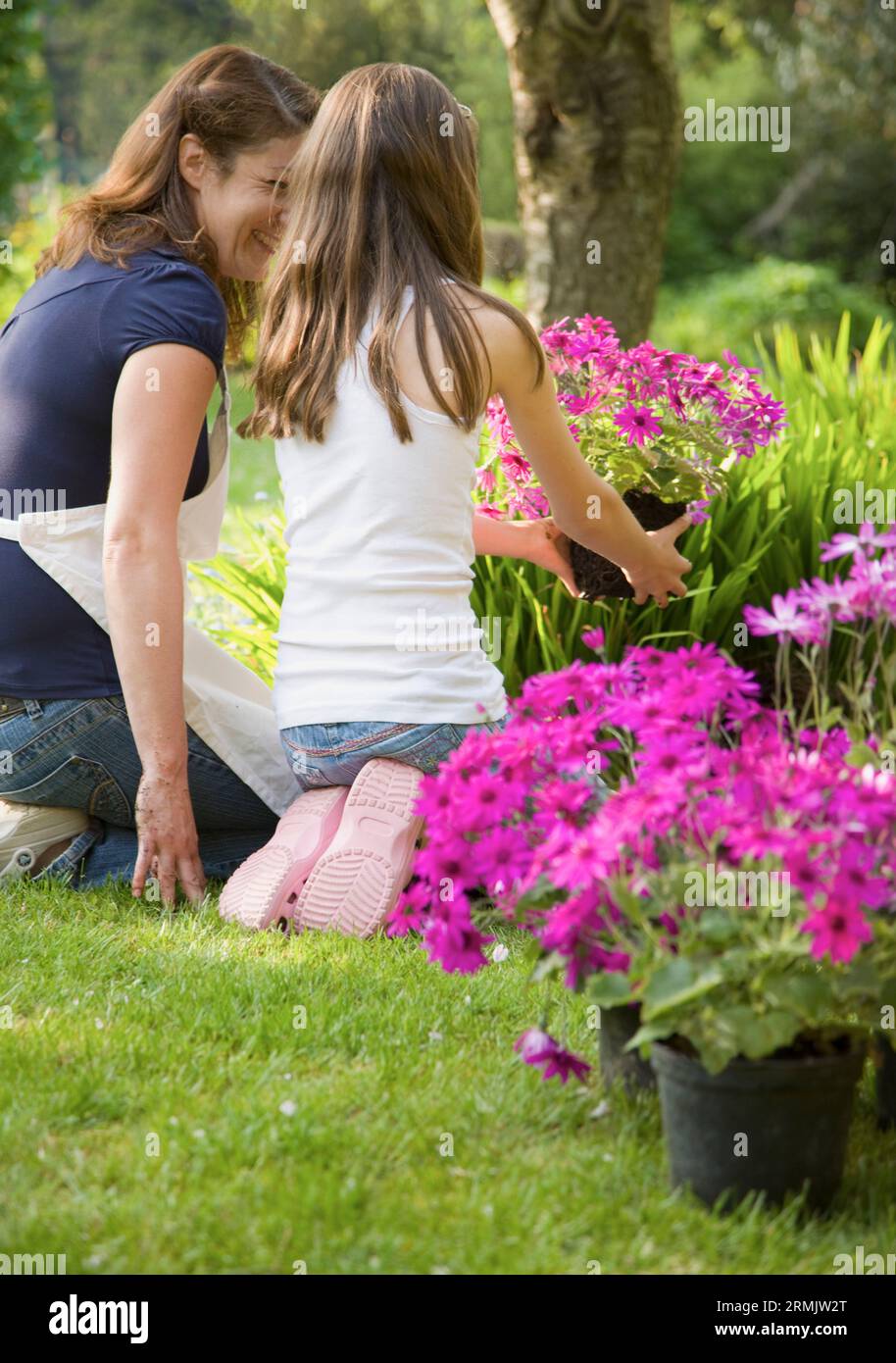 Retro della madre e figlia in ginocchio in giardino tendente piante e sorridente Foto Stock