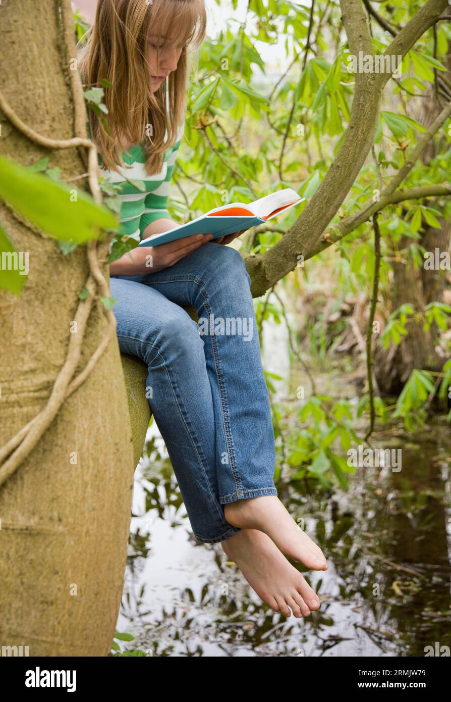 Ragazza adolescente seduta su un albero che legge un libro Foto Stock