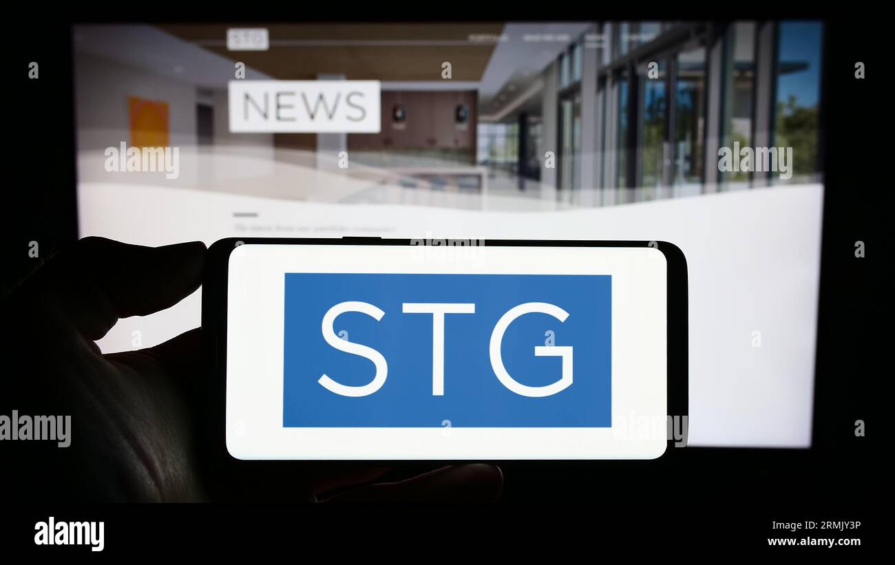 Persona in possesso di un cellulare con il logo della società di private equity statunitense STG Partners LLC sullo schermo davanti alla pagina Web aziendale. Concentrarsi sul display del telefono. Foto Stock