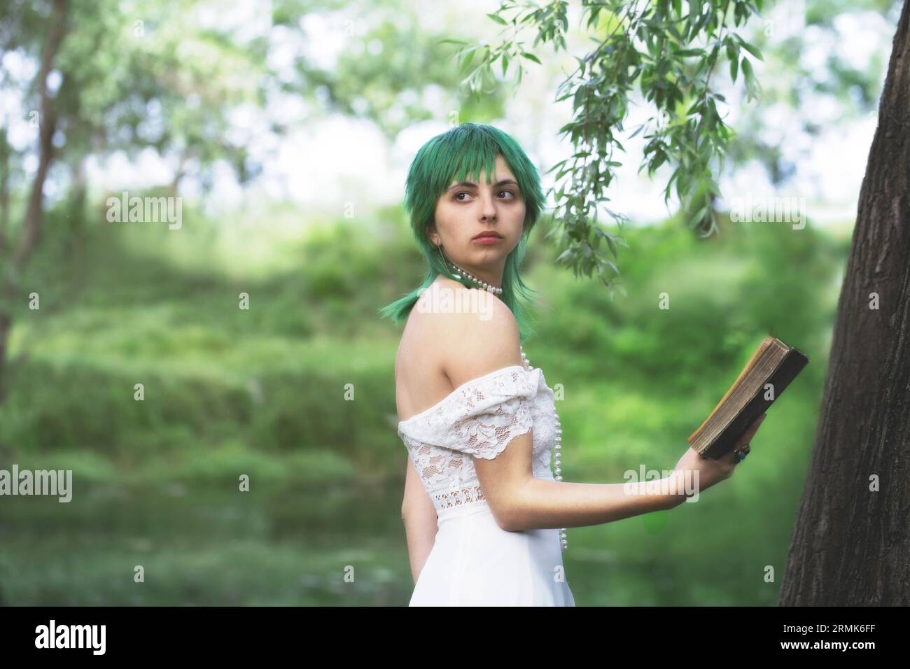 elegante ragazza dai capelli verdi che legge un libro nella quiete di un parco verde donne in un'atmosfera verde e surreale Foto Stock
