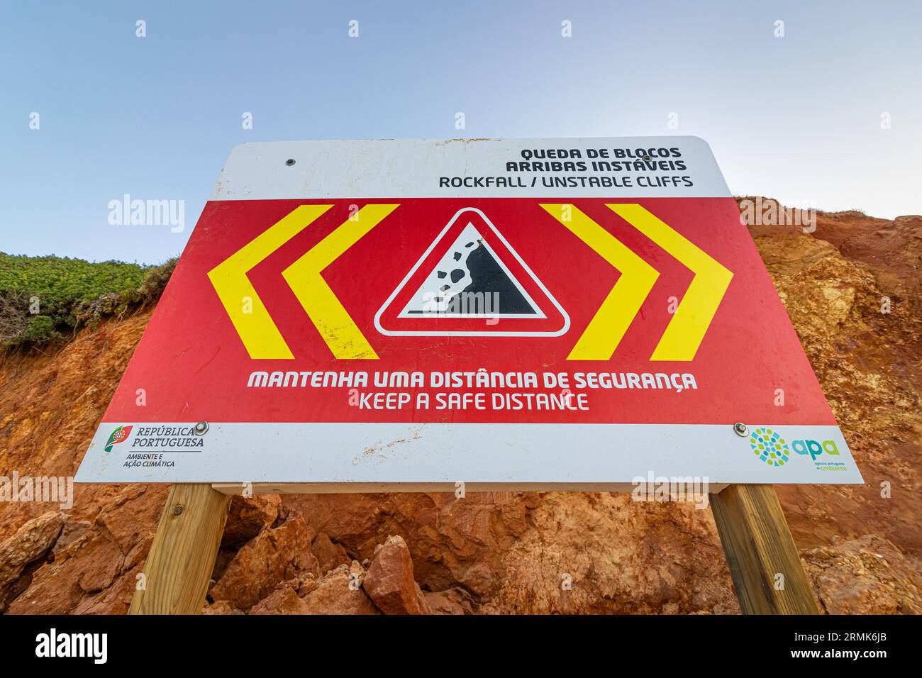 SCOGLIERE INSTABILI A CADUTA ROCCIOSA, MANTENERE Una DISTANZA DI SICUREZZA è scritto in inglese su un cartello di avvertimento in Portogallo sulle scogliere dell'Oceano Atlantico. Rocce e. Foto Stock