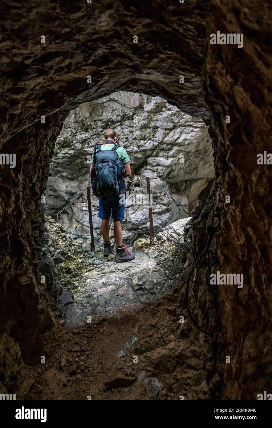 Alpinista sulla strada attraverso l'Hoellentalklamm, all'uscita di una grotta, stretta gola di roccia con ruscello di montagna, montagne Wetterstein Foto Stock