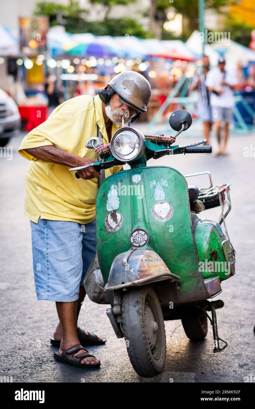 Un vecchio tailandese mette in pausa la sua classica vespa verde su Yaowarat Rd. China Town, Bangkok, Thailandia. Foto Stock