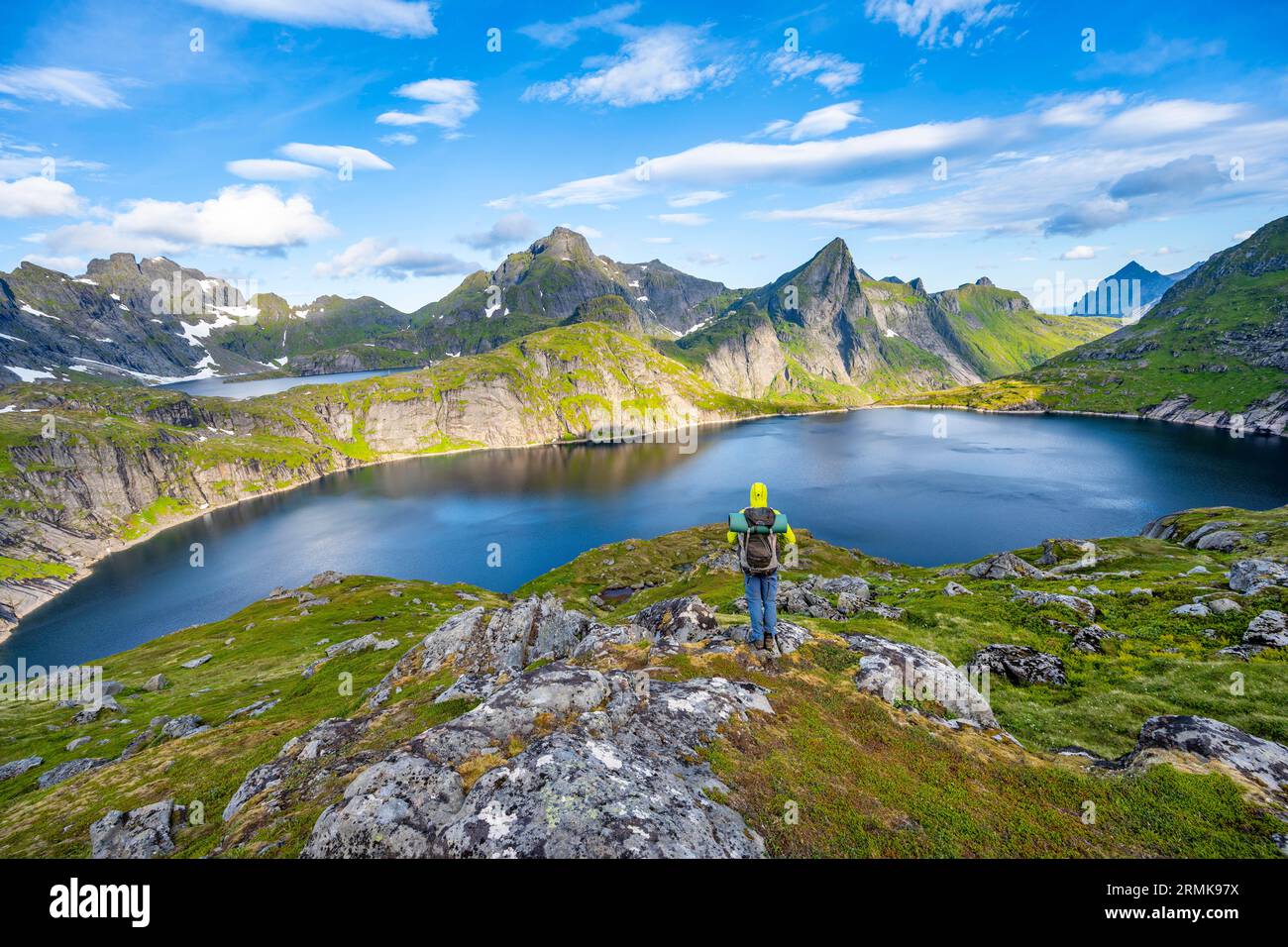 Alpinista che guarda al lago, paesaggio montano con il lago Tennesvatnet, all'alba, dietro la vetta di Hermannsdalstinden, Moskenesoya, Lofoten Foto Stock