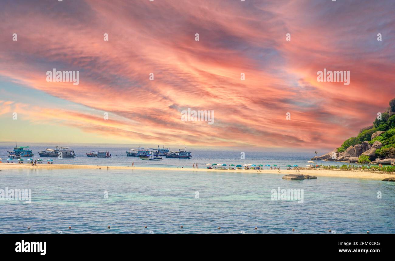 Sottile striscia di spiaggia a Ko Tao Thailandia, dove i ricchi turisti vengono a prendere il sole, e sullo sfondo è possibile vedere le barche da pesca e le immersioni subacquee e un cielo rosso Foto Stock