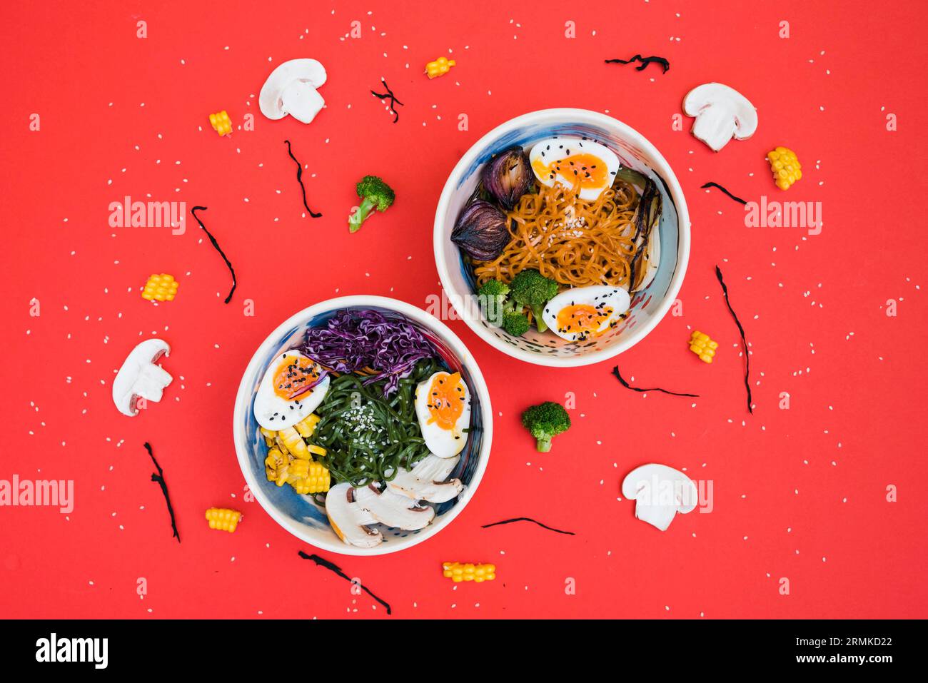 Ciotole di ramen speziate con noodles uova sode e verdure servite con insalata di alghe sullo sfondo rosso Foto Stock