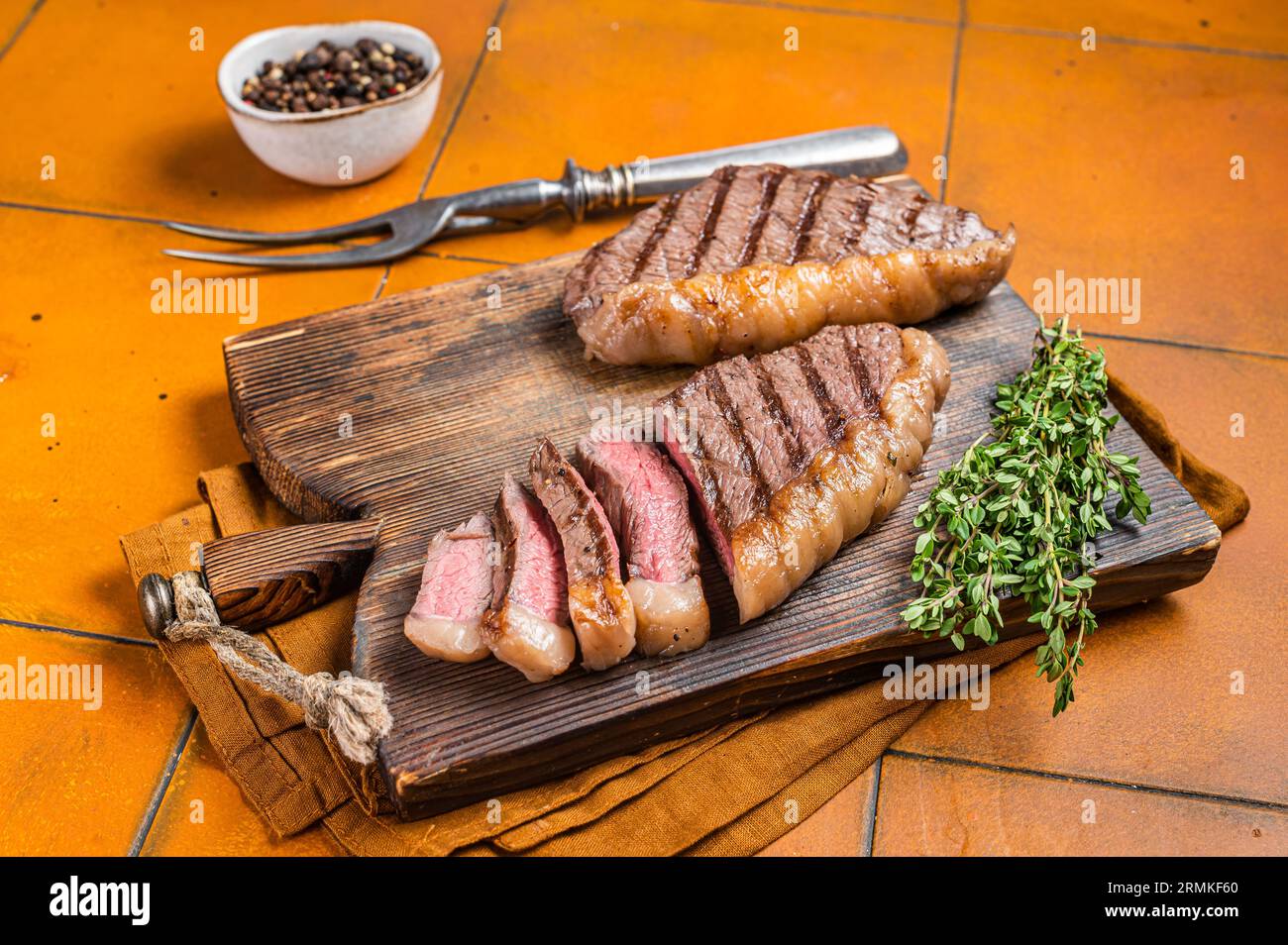 Barbecue arrosto bistecca di Picanha brasiliana, bistecca di carne di manzo di coppa su un tavolo di servizio in legno. Sfondo arancione. Vista dall'alto. Foto Stock
