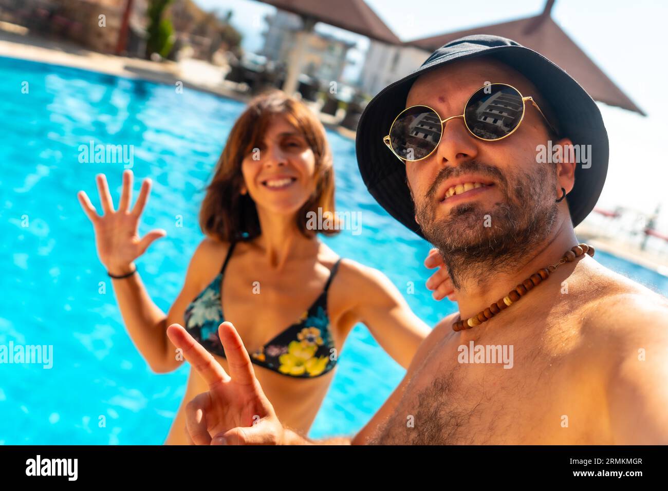 Una coppia turistica nella piscina dell'hotel in estate si prende un selfie godendosi la vacanza Foto Stock