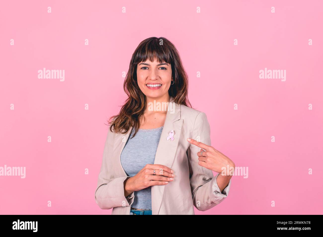 Donna sorridente che indossa un nastro rosa per la consapevolezza del cancro al seno mentre lo indica Foto Stock
