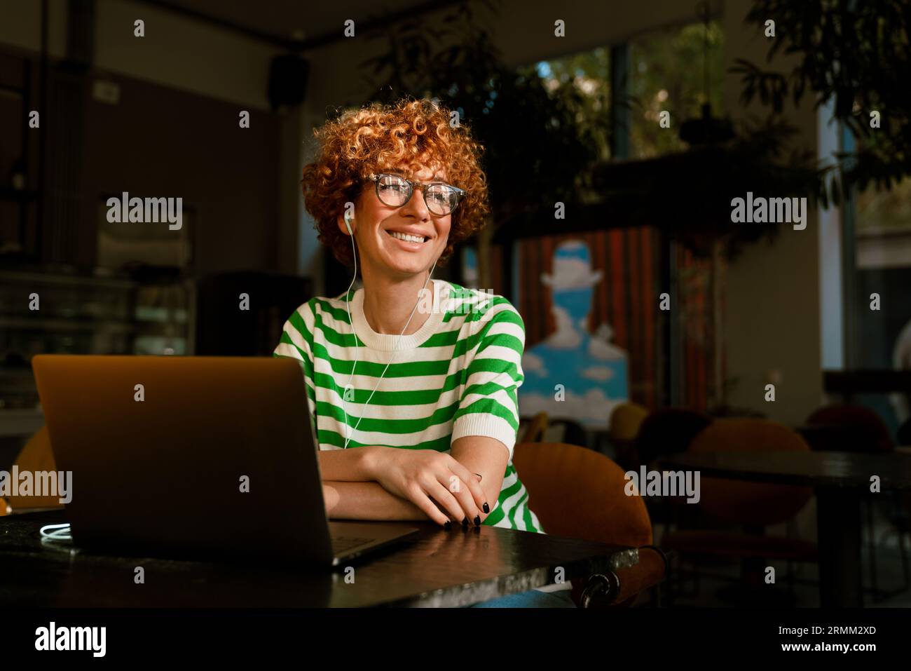 Donna di colore bianco medio con capelli ricci che utilizza un computer portatile mentre si siede al tavolo in una caffetteria Foto Stock